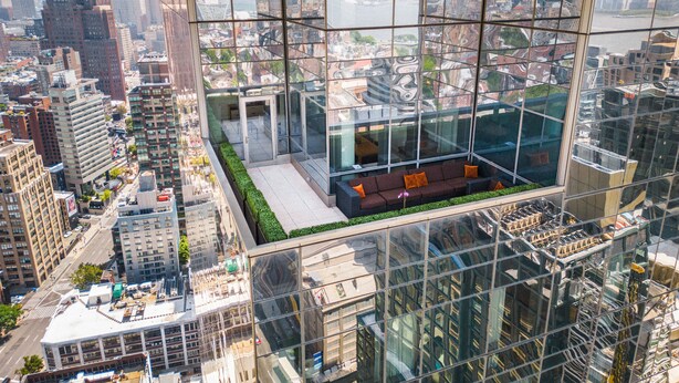 Un immeuble de grande hauteur doté d’une façade en verre, d’un jardin sur le toit et d’un espace détente avec des coussins.