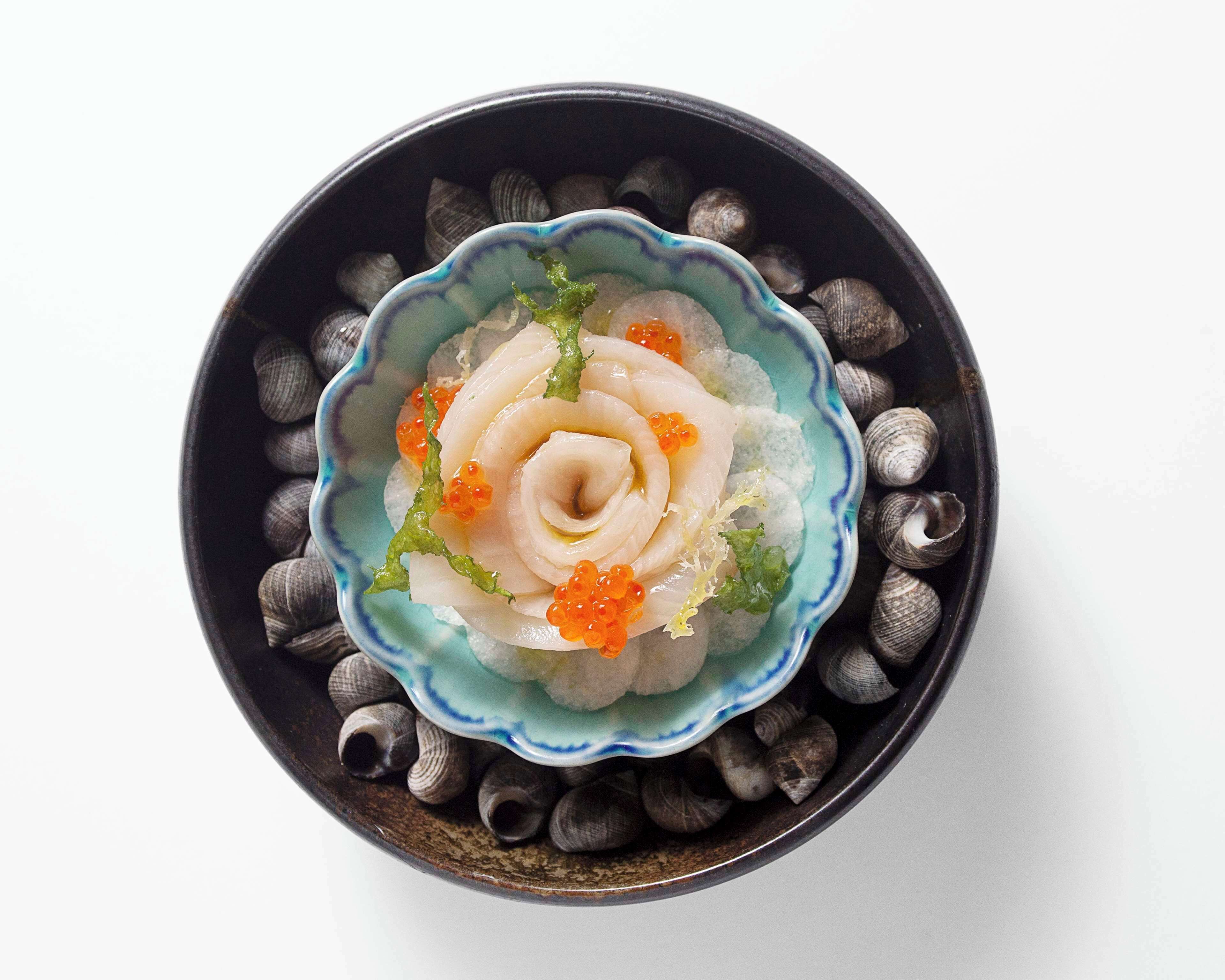A bowl of sashimi with roe and garnishes on a plate surrounded by seashells.