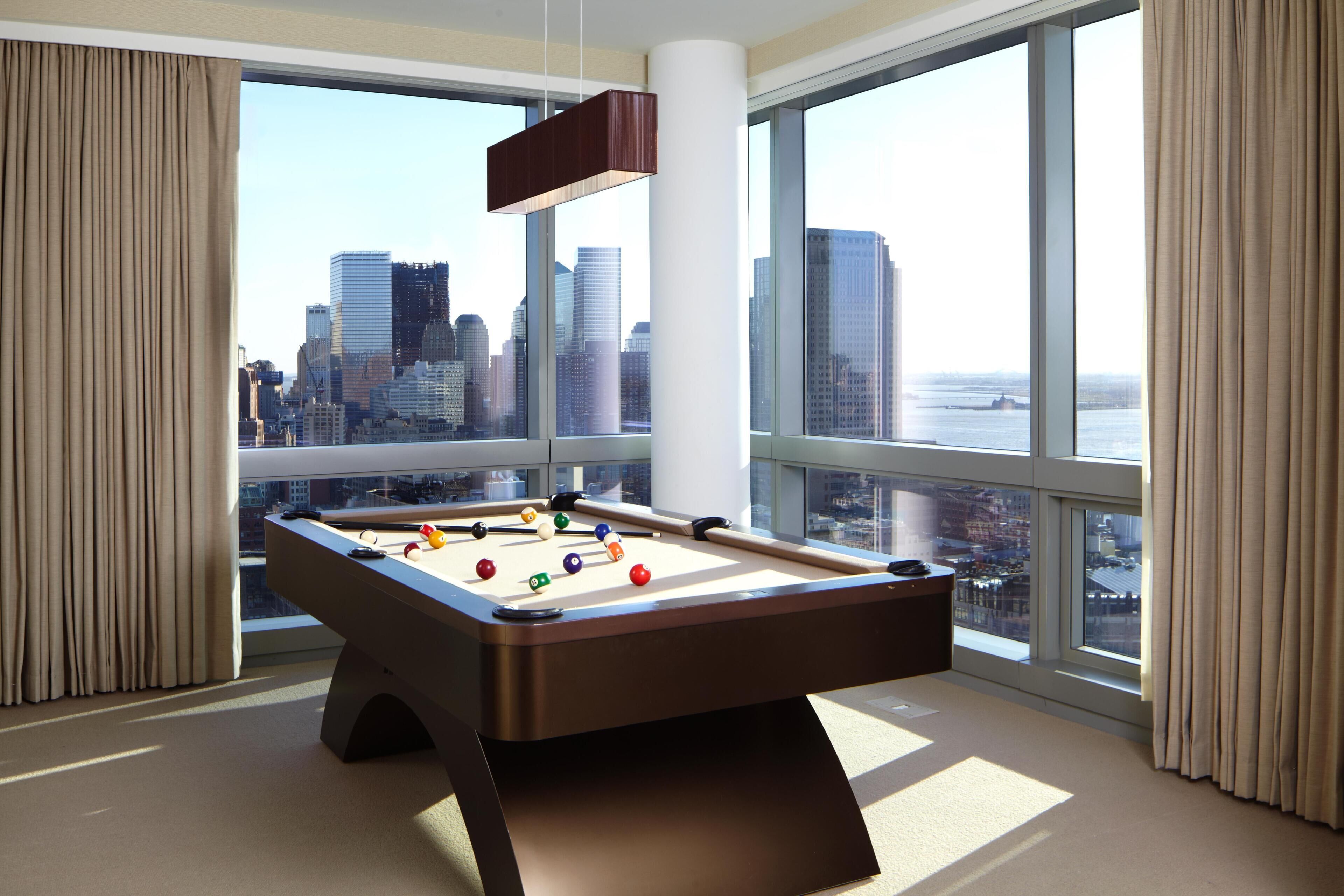 A pool table in a room with large windows overlooking a cityscape.