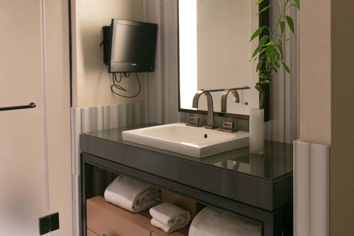A modern bathroom with a large mirror, a sink, a flat-screen TV, and a plant.