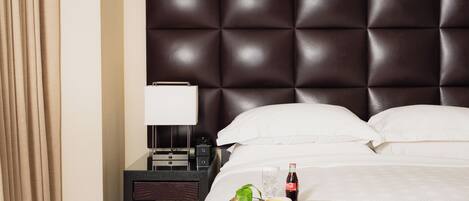 A hotel room with a tufted headboard, a bedside table with a lamp, and a tray with breakfast items.