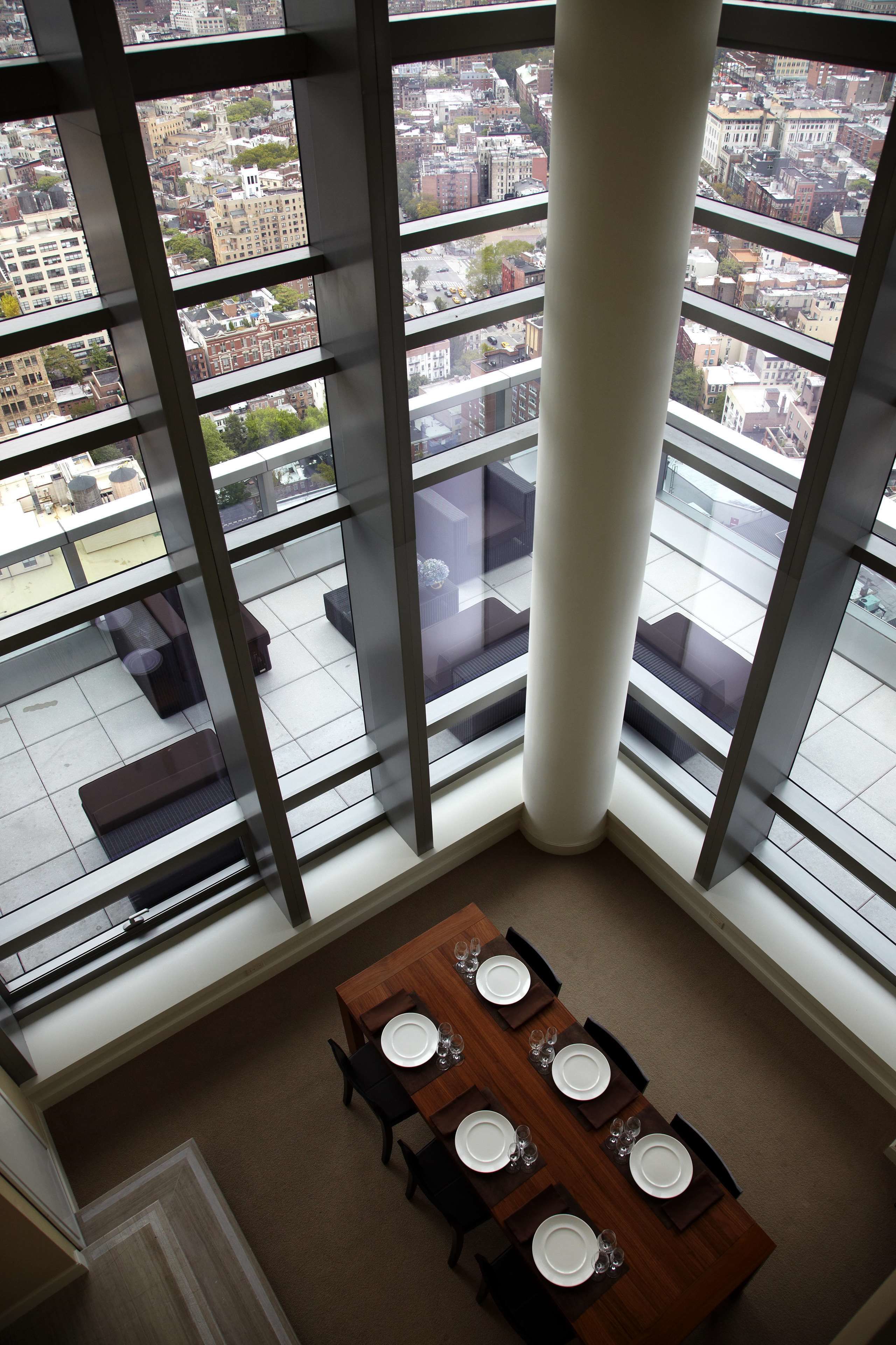Un comedor con una mesa lista para cuatro personas, ventanas amplias que ofrecen vista a la ciudad y un techo alto con una columna central.