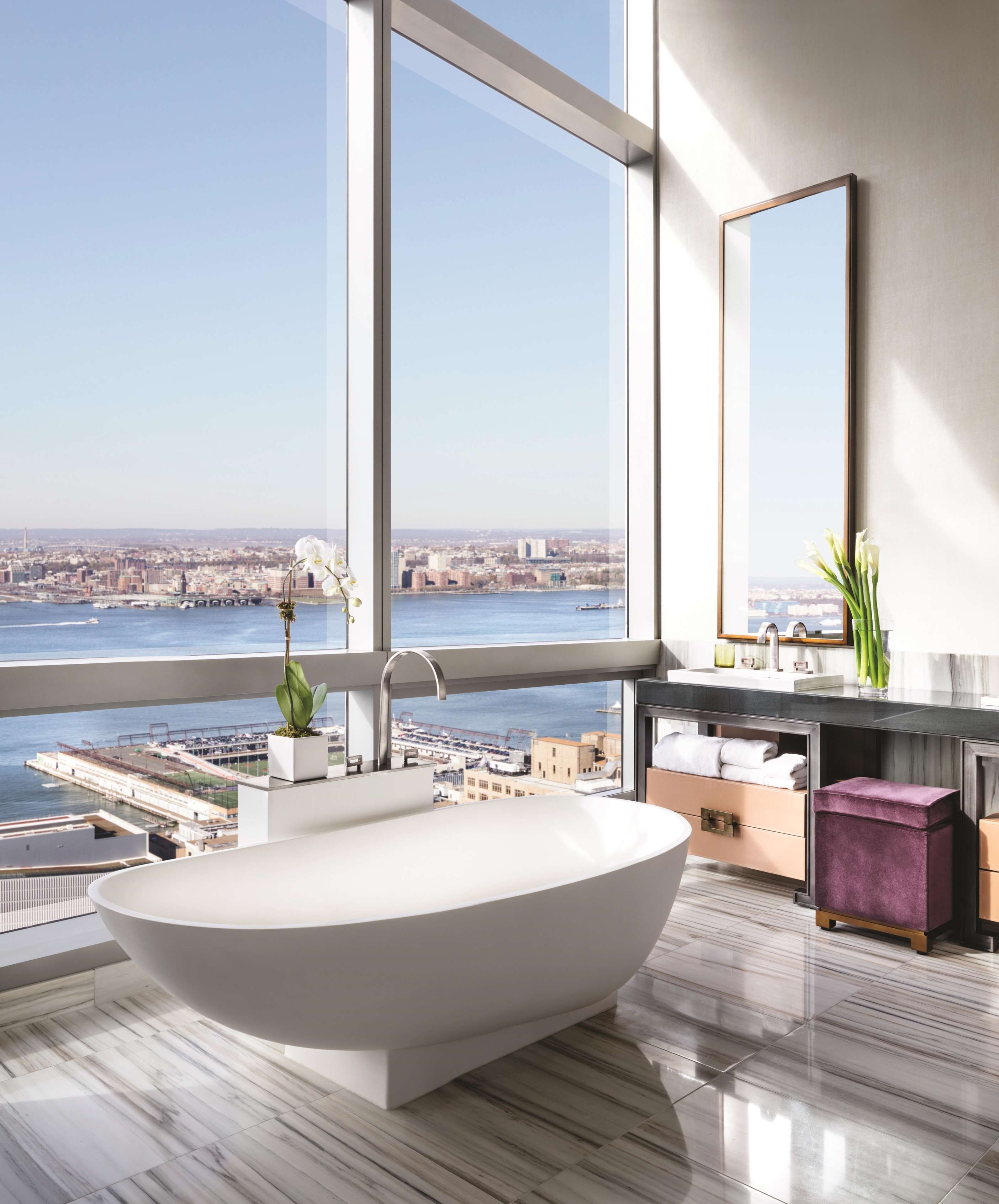 Une salle de bain moderne avec une baignoire sur pieds, une grande fenêtre donnant sur la ville et un meuble-lavabo avec un miroir.