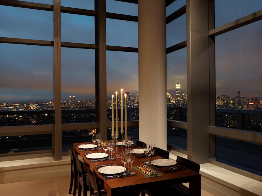 Une table à manger dressée pour six personnes, décorée de bougies, avec vue sur le paysage urbain au crépuscule.