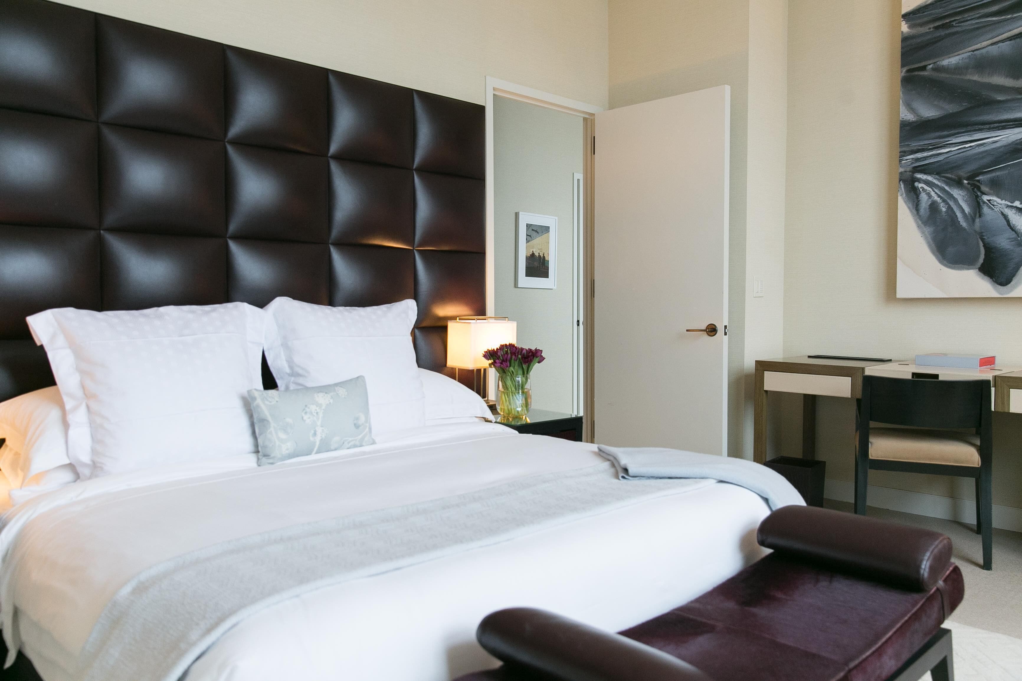 Una habitación de hotel con una cama grande, una mesita de noche con lámpara, un escritorio y una silla.