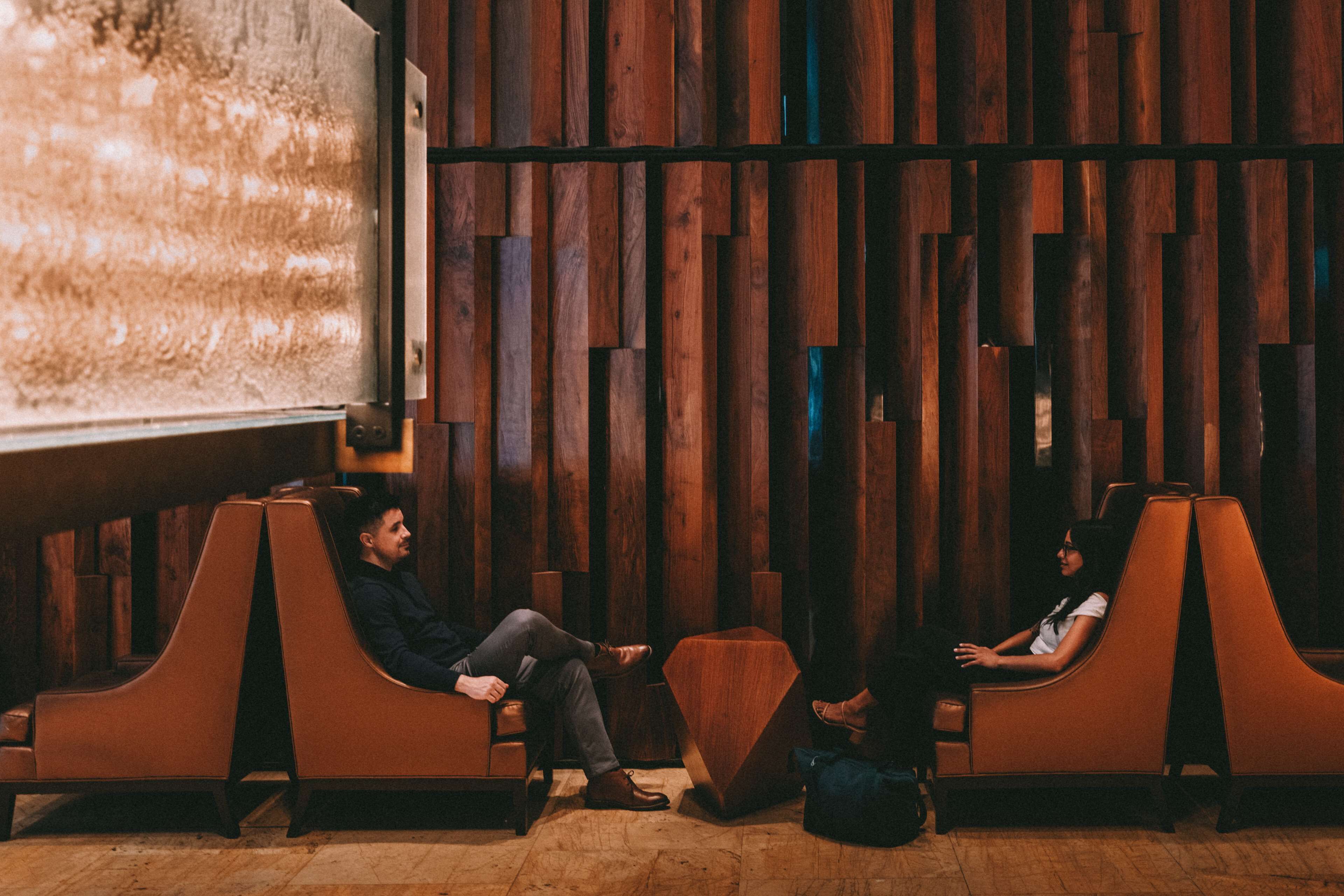 A room with a wooden slat wall, two leather armchairs, and a projection screen.