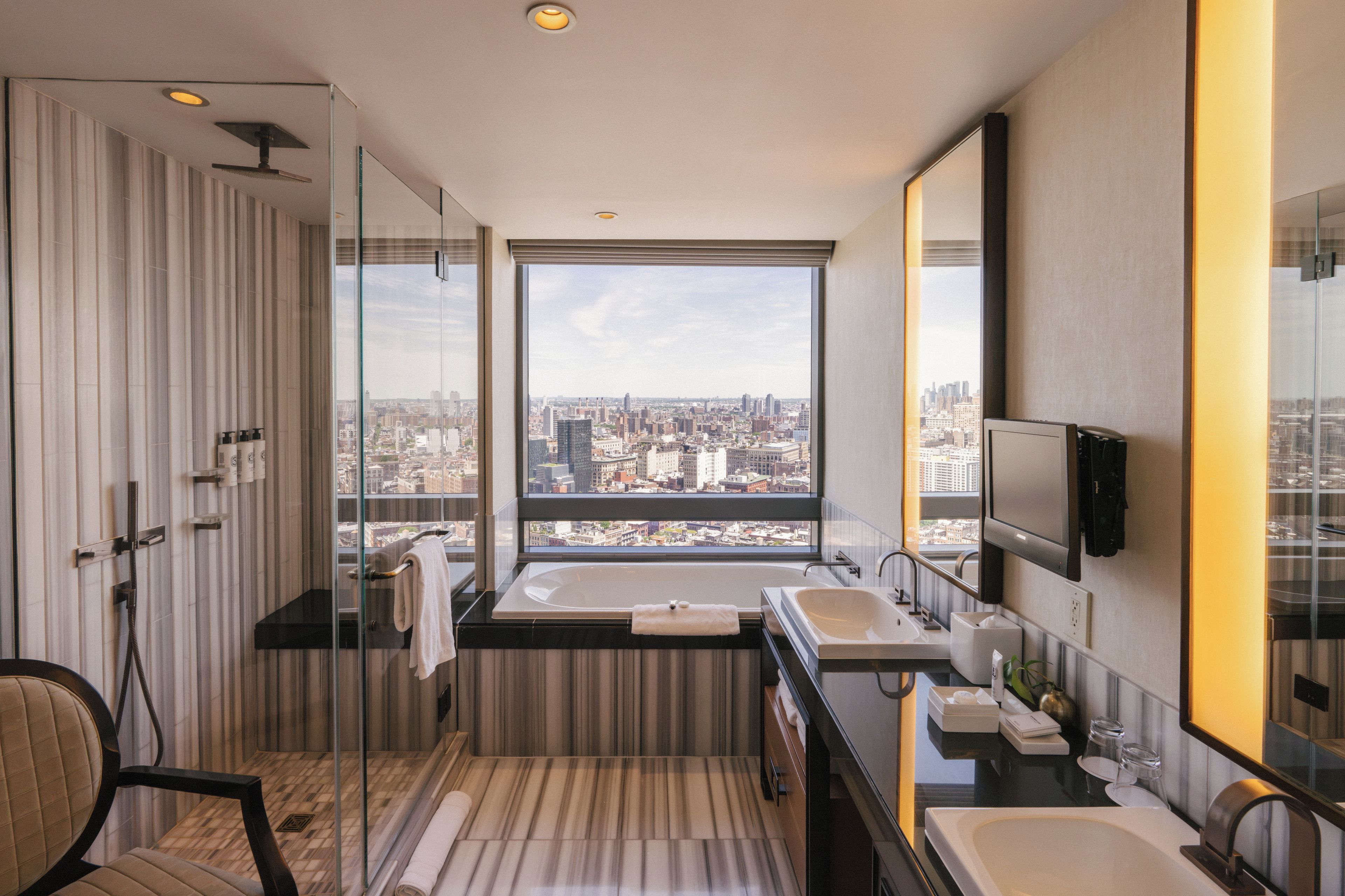 A modern bathroom with a large window, a bathtub, a shower, and a vanity with a mirror.