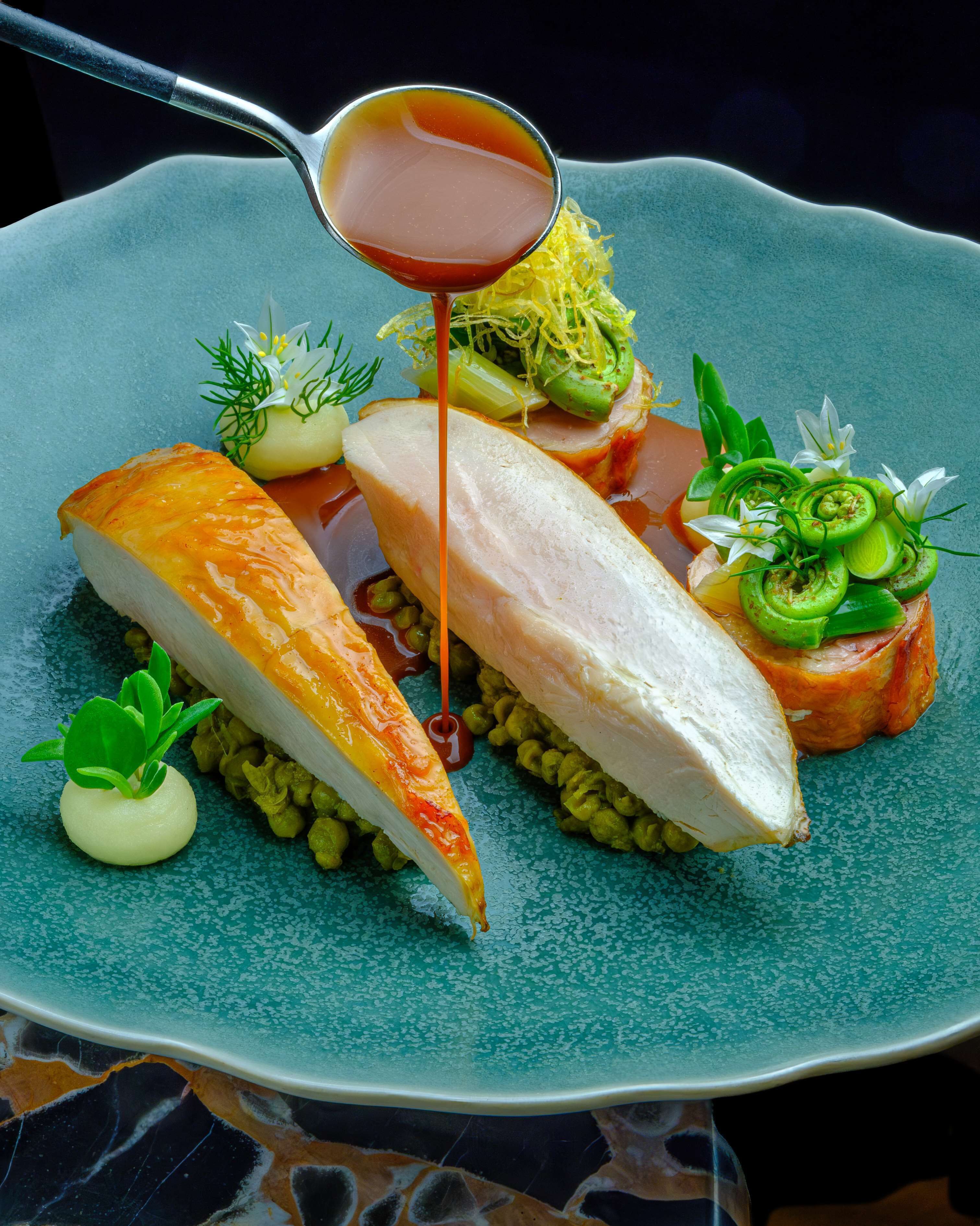 A plate of food with various items including a slice of salmon, a piece of white meat, and some garnishes.