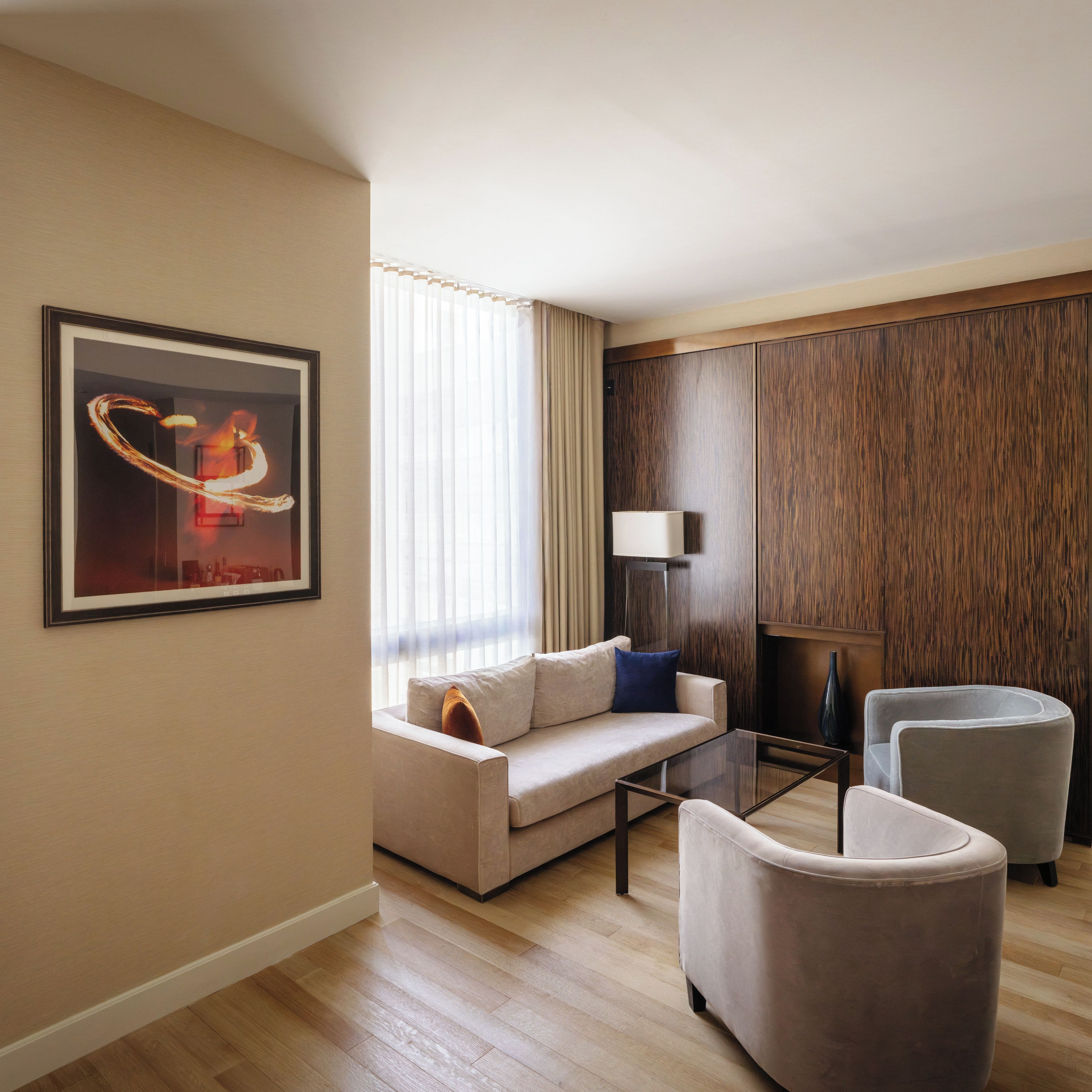 Una habitación de hotel moderna con sofá, sillones, una mesita de centro y una obra de arte enmarcada en la pared.