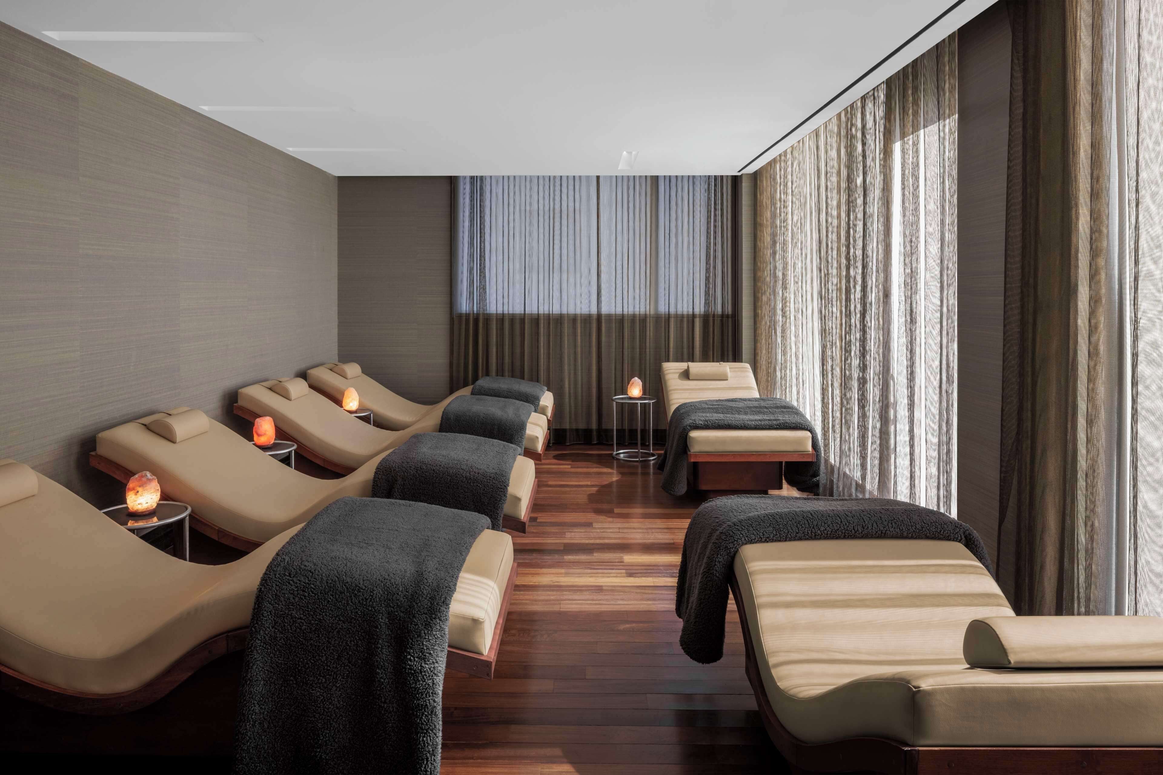 A spa room with multiple massage chairs, a small table with a candle, and a large window with curtains.