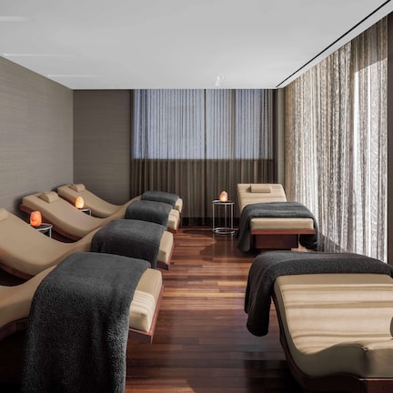 A spa room with multiple massage chairs, a small table with a candle, and a large window with curtains.