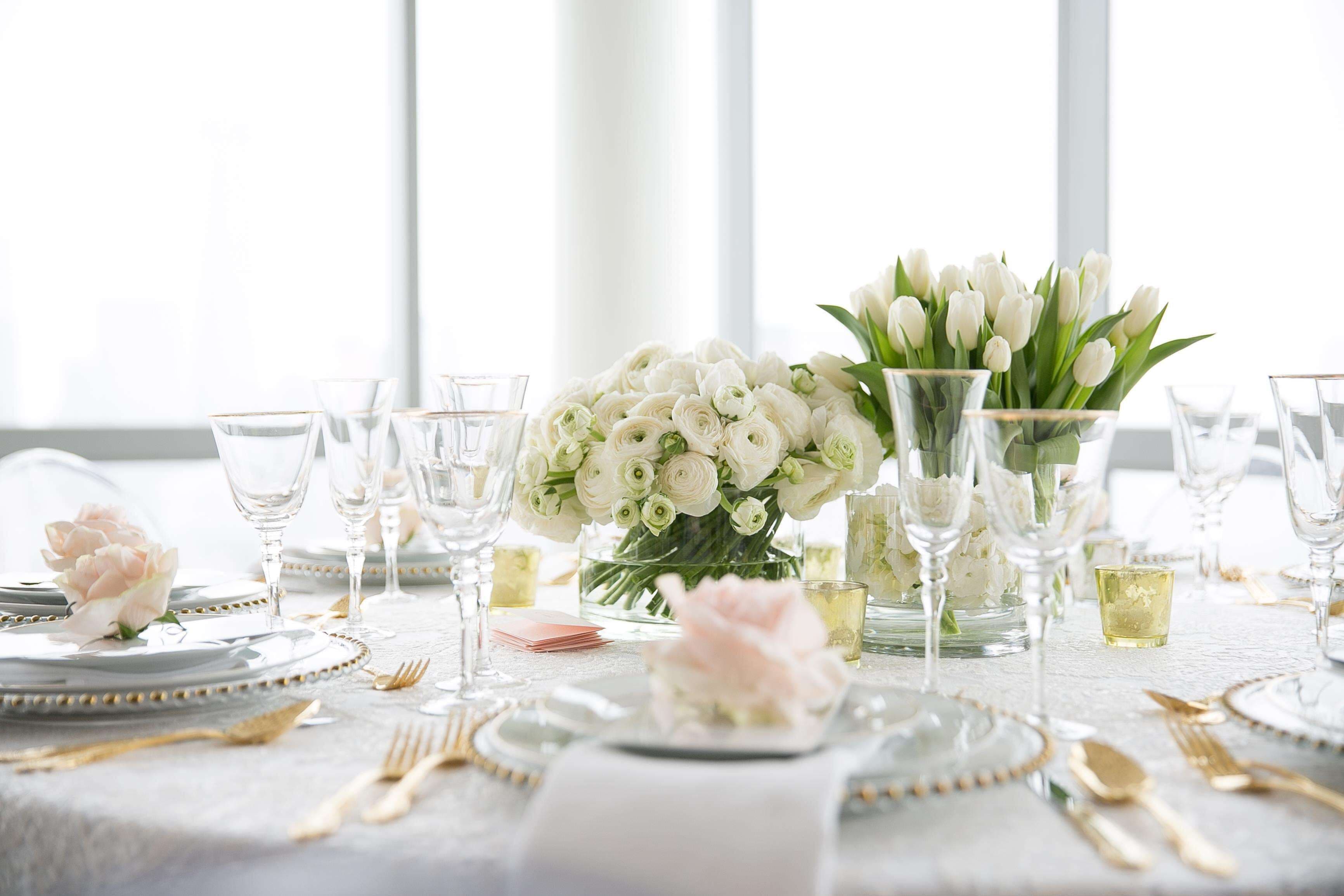 A table set for a formal event with white tablecloths, clear glassware, and a centerpiece of white flowers.