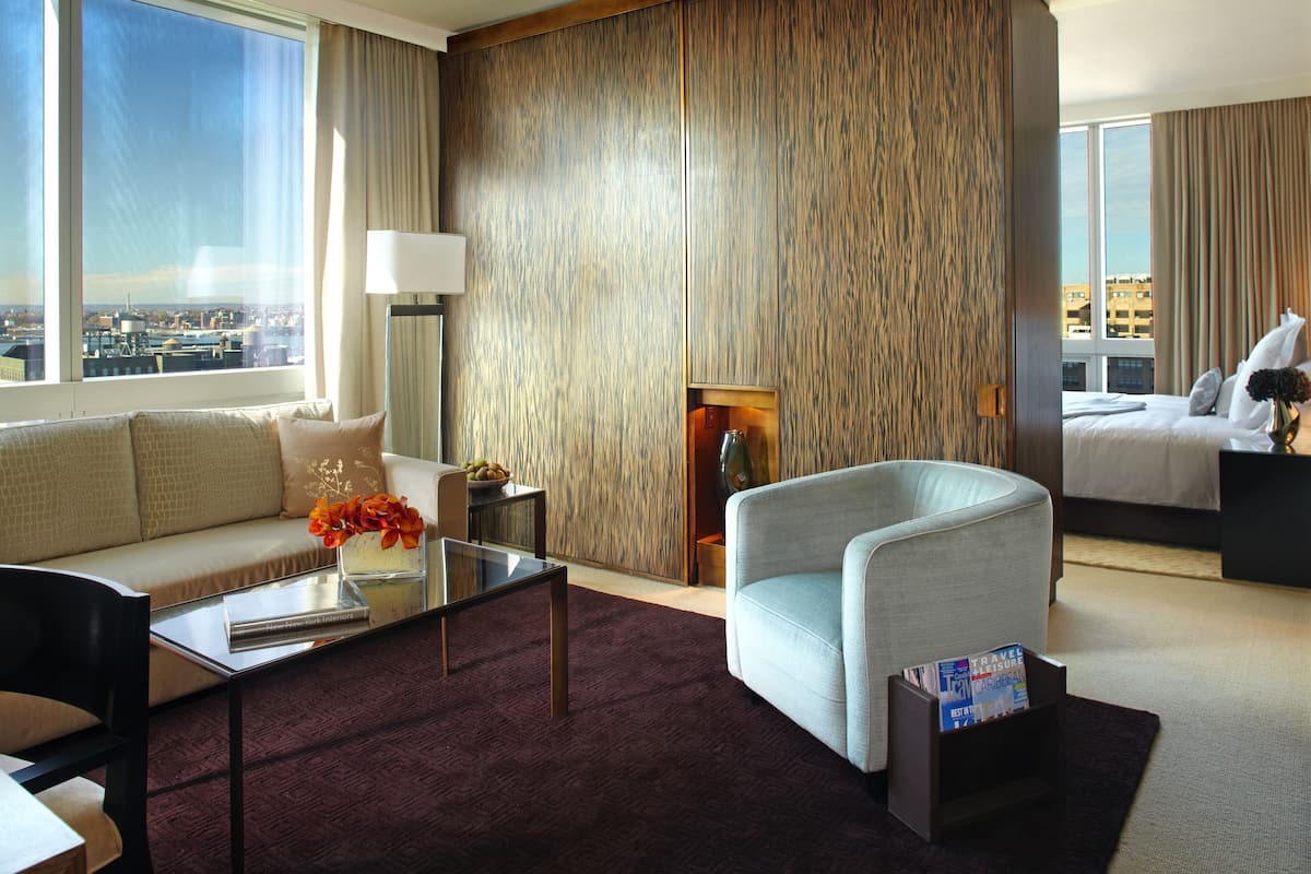 A hotel room with a sofa, armchair, and a small table with a vase and flowers.