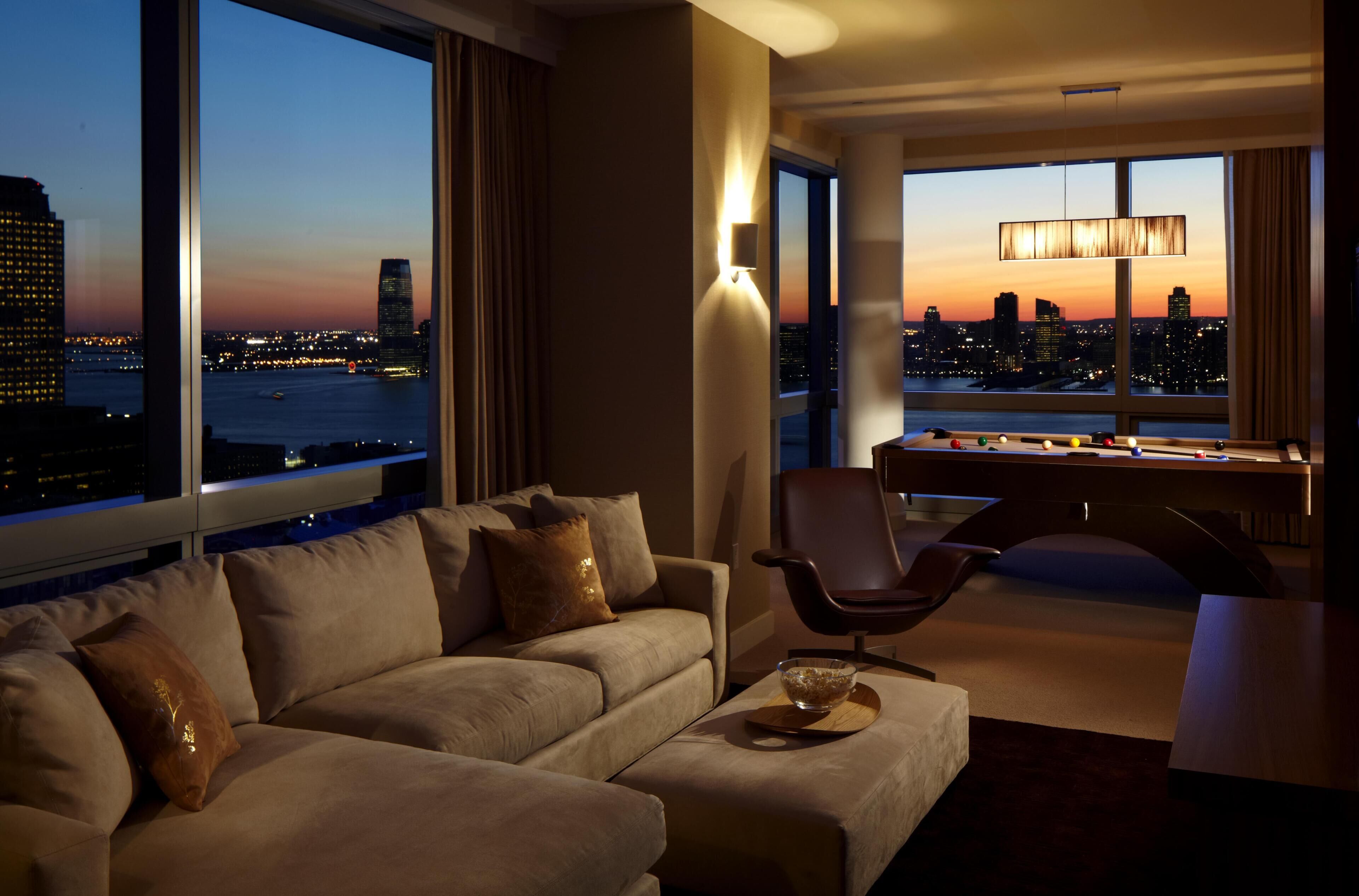Een moderne hotelkamer met een bank, een bureau en uitzicht op de stad in de schemering.