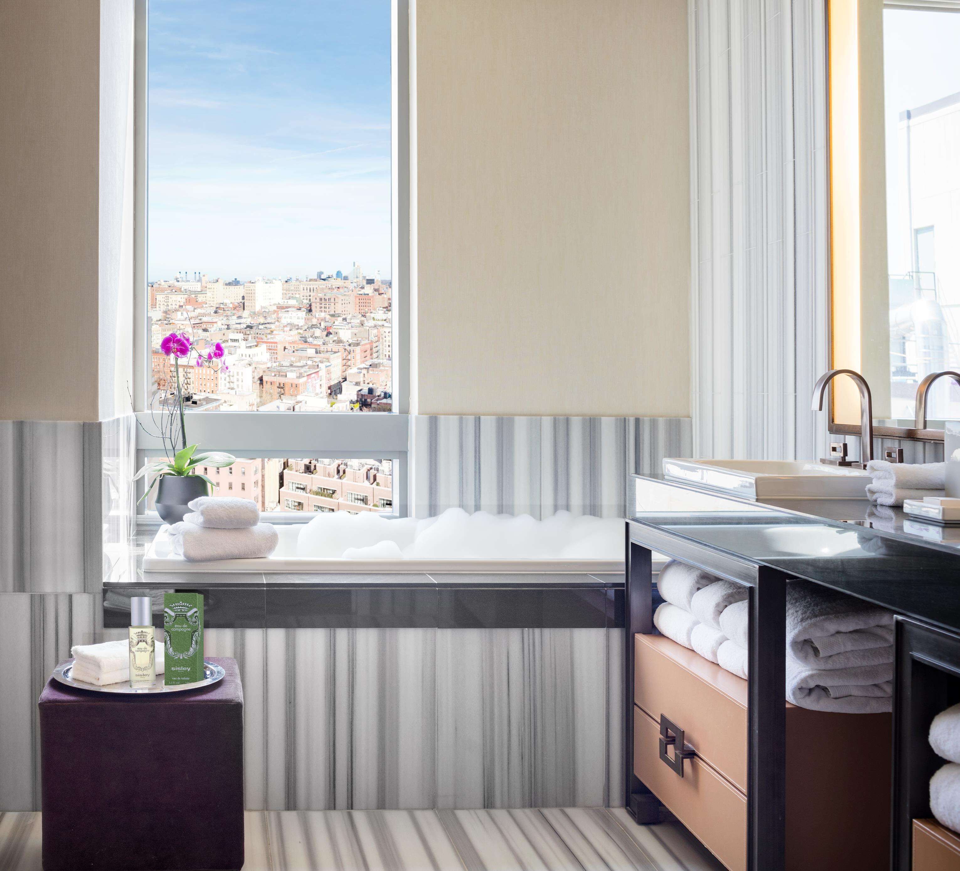 A modern bathroom with a large window, a bathtub, a vanity with a mirror, and a towel rack.