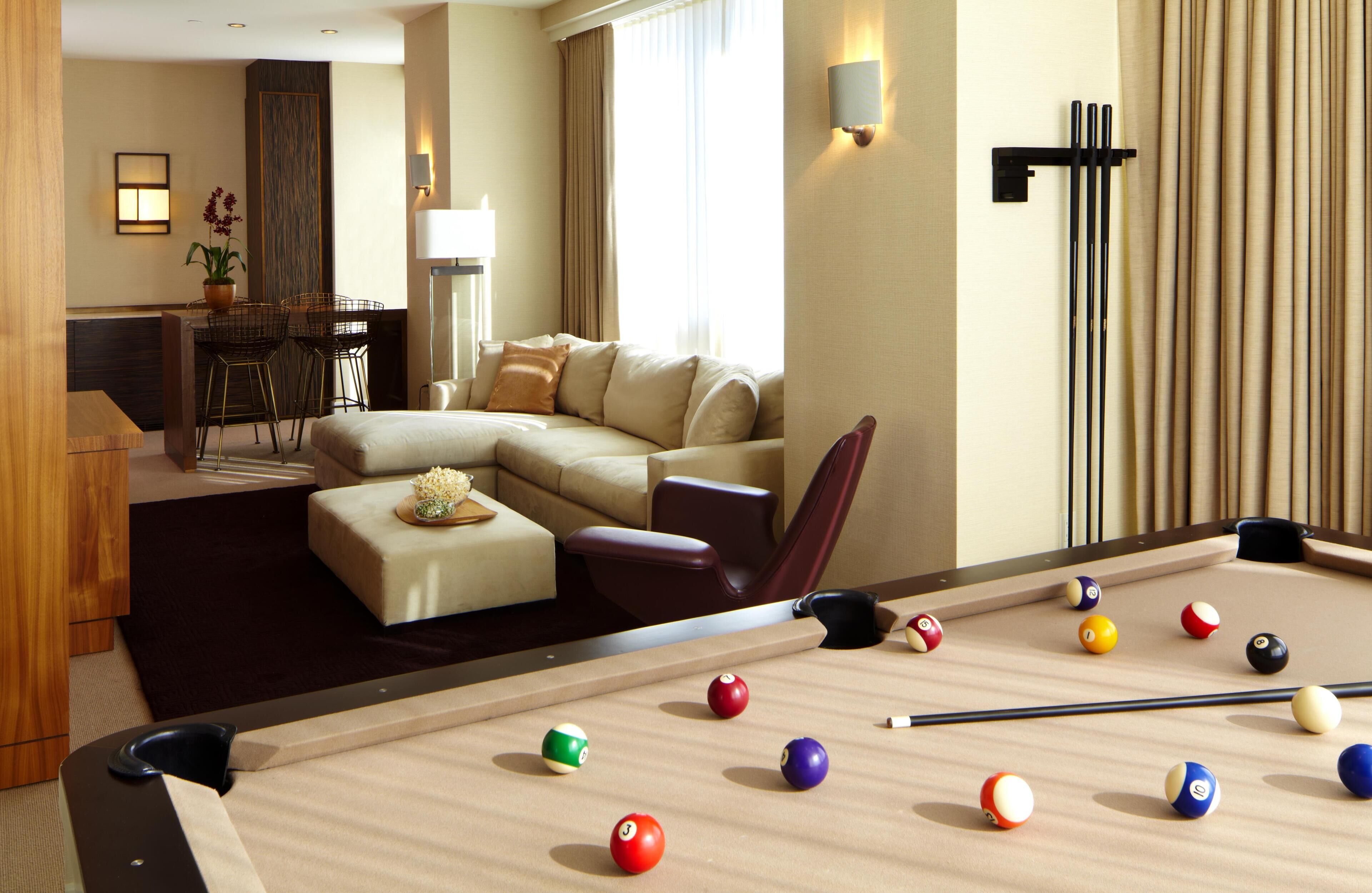 A hotel room with a pool table, a sofa, a dining area, and a lamp.