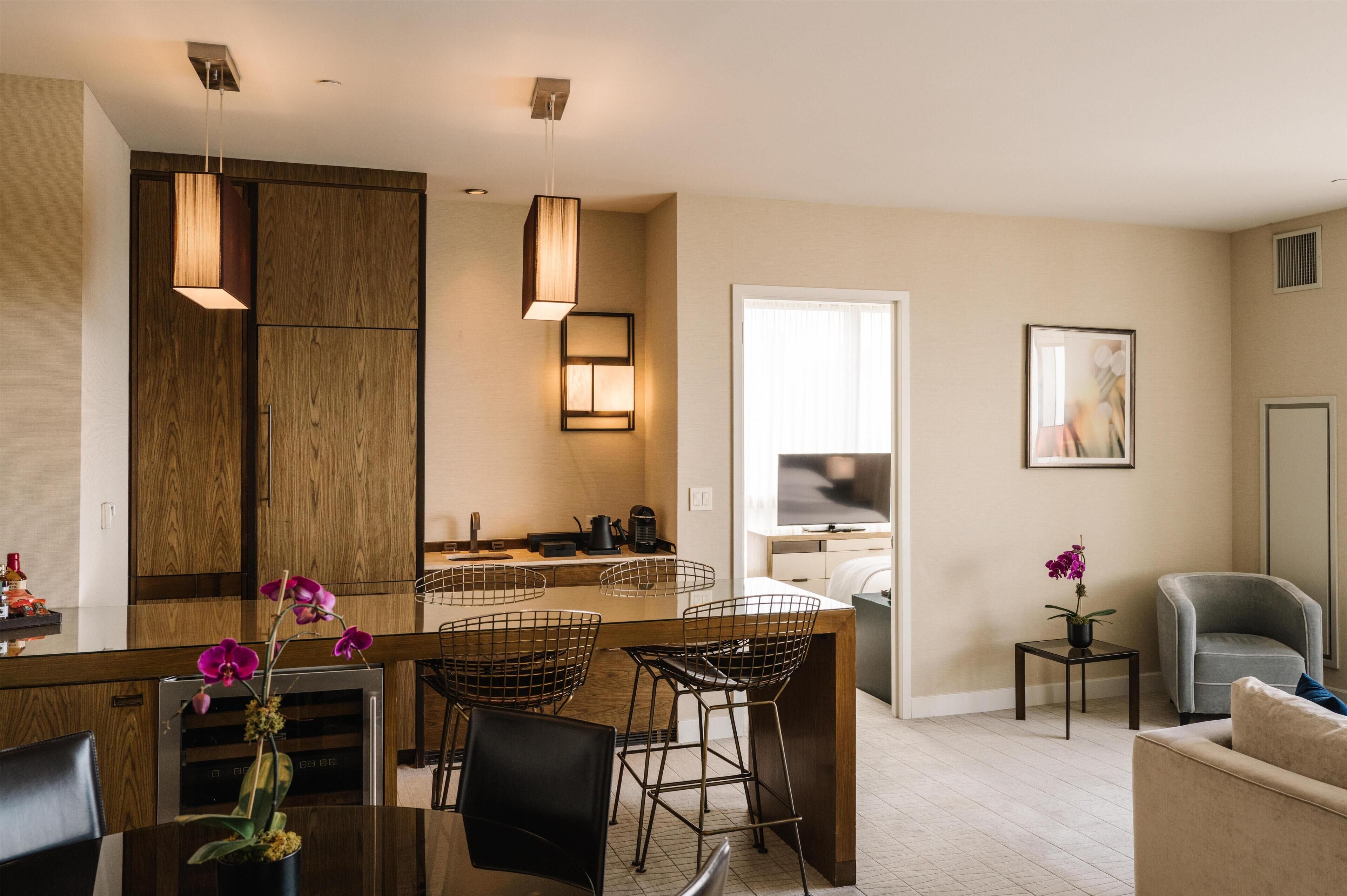 A modern kitchen with wooden cabinets, pendant lights, and a dining area with metal chairs.
