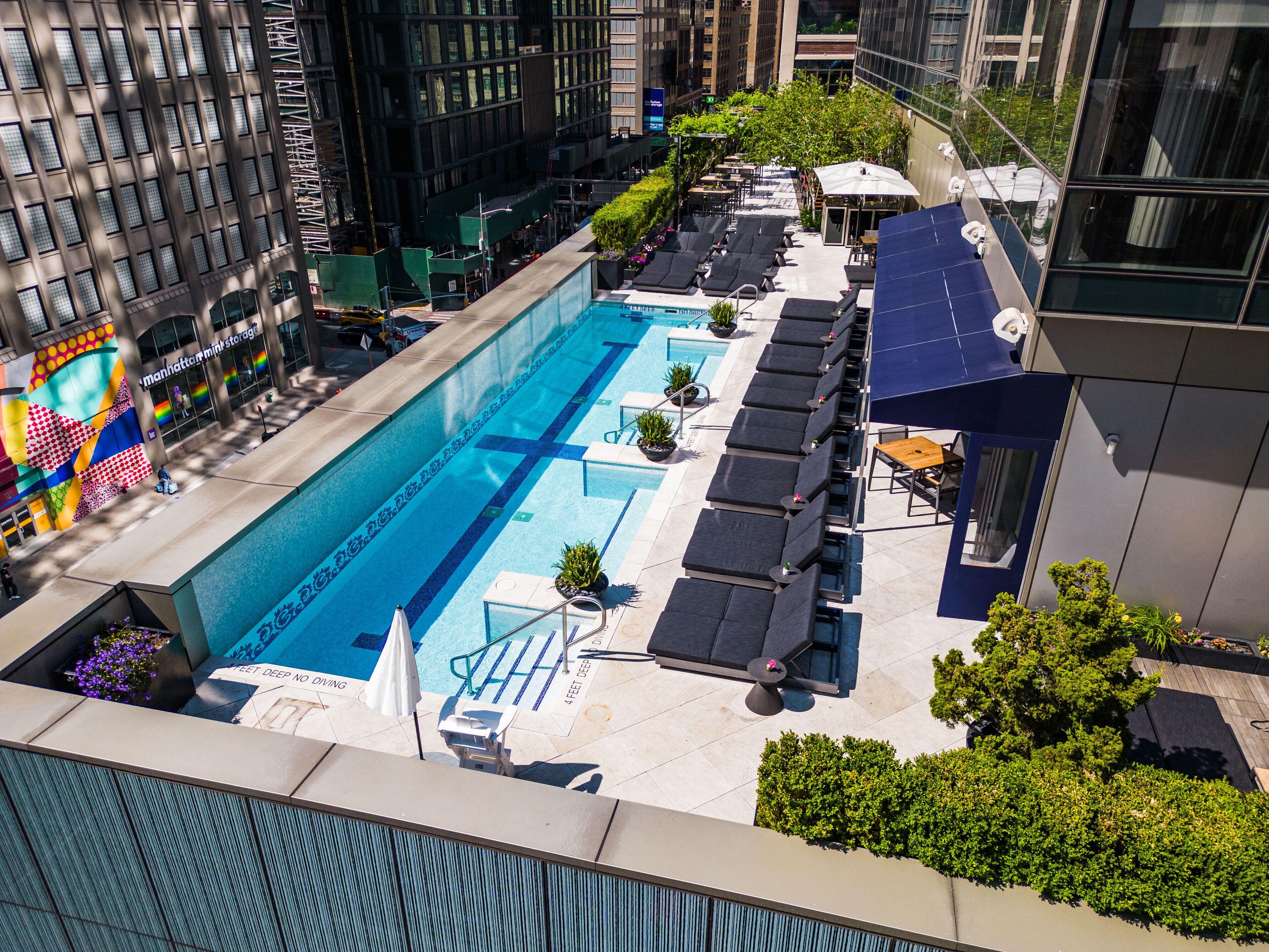 A rooftop pool with lounge chairs and a bar area, surrounded by high-rise buildings.
