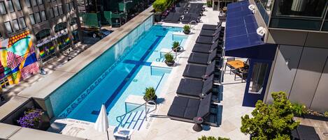 A rooftop pool with lounge chairs and a bar area, surrounded by high-rise buildings.
