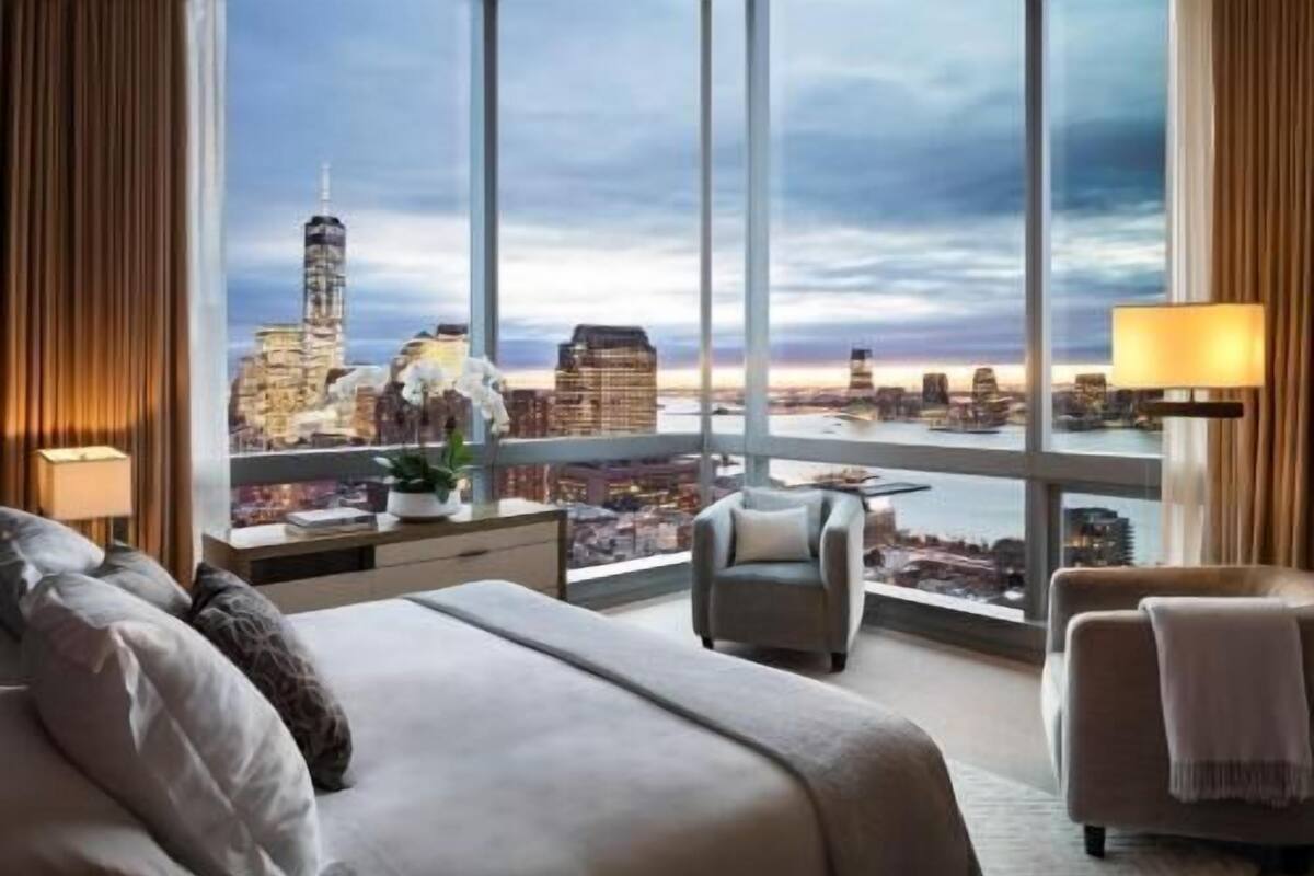 A hotel room with a large bed, a desk, a chair, and a view of a cityscape.