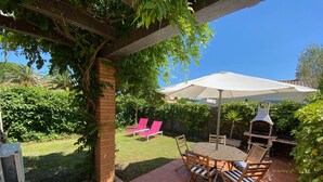Um pátio com um pilar de tijolos, uma mesa com cadeiras, churrasqueira e um guarda-sol coberto.