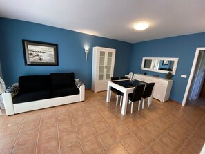 A living room with a black and white sofa, a dining table with chairs, a white cabinet, and a framed picture on the wall.