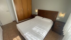 Quarto com cama, guarda-roupa de madeira, mesas de cabeceira e luzes fixadas na parede.