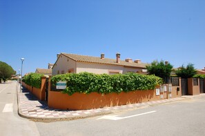 Un edificio a due piani con tetto in tegole, un marciapiede lastricato e un siepe verde davanti.
