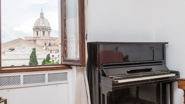 A piano in a room with a window overlooking a building with a dome and columns. - Ancient Rome View Apartment (Rome)