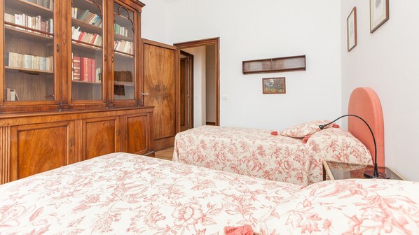 Une chambre avec deux lits, une armoire en bois remplie de livres et un petit tableau accroché au mur.