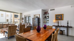 A spacious living area with a wooden dining table, wicker furniture, and a large window offering a view of the city. - Espigon Central - Punta del Moral Beach PEHC14P79 (Punta del Moral)