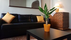 A living room with a black leather sofa, two mustard-colored cushions, a small table, a potted plant, a lamp, and a wooden cabinet. - Spacious and Beautiful 60 sqm Apartment in the Very Heart of Bologna (Bologna)
