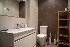 Un baño moderno con un lavamanos blanco, un inodoro y una estantería de madera.