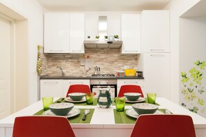 A modern kitchen with white cabinets, a tiled backsplash, and a dining area with red chairs and green placemats. - Large and completely refurbished apartment with a beautiful patio. (Firenze)