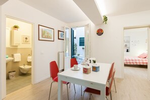 A modern interior with a dining area, a visible bathroom, and a bedroom with a checkered bedspread. - Large and completely refurbished apartment with a beautiful patio. (Firenze)