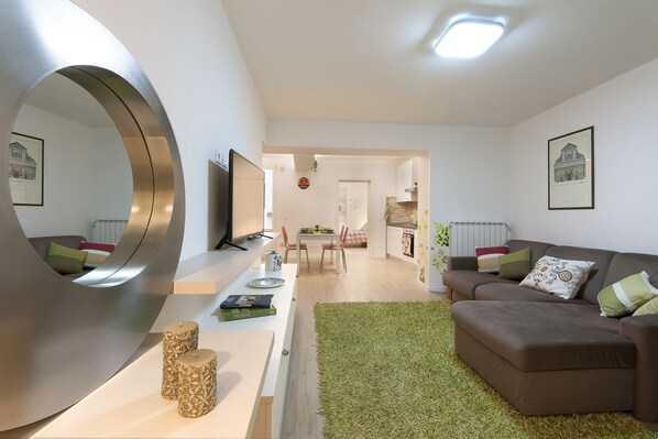 A modern living room with a large mirror, a brown sofa, a dining area, and a kitchen in the background. - Large and completely refurbished apartment with a beautiful patio. (Firenze)