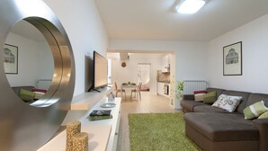 A modern living room with a large mirror, a brown sofa, a dining area, and a kitchen in the background. - Large and completely refurbished apartment with a beautiful patio. (Firenze)