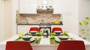 A modern kitchen with white cabinets, a tiled backsplash, and a dining table set with green placemats and bowls. - Large and completely refurbished apartment with a beautiful patio. (Firenze)