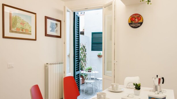 A dining area with a table set for two, a radiator, a red chair, and a door leading to an outdoor space with a table and chairs. - Large and completely refurbished apartment with a beautiful patio. (Firenze)