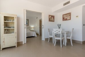 A room with a bed, a dining table with chairs, a cabinet with glass doors, and two framed pictures on the wall.