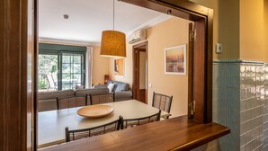 A dining area with a wooden table and chairs, a hanging light fixture, and a view of a living room with a sofa and a window. - Prado Golf - Isla Canela Golf GPHG45P86 (Isla Canela)