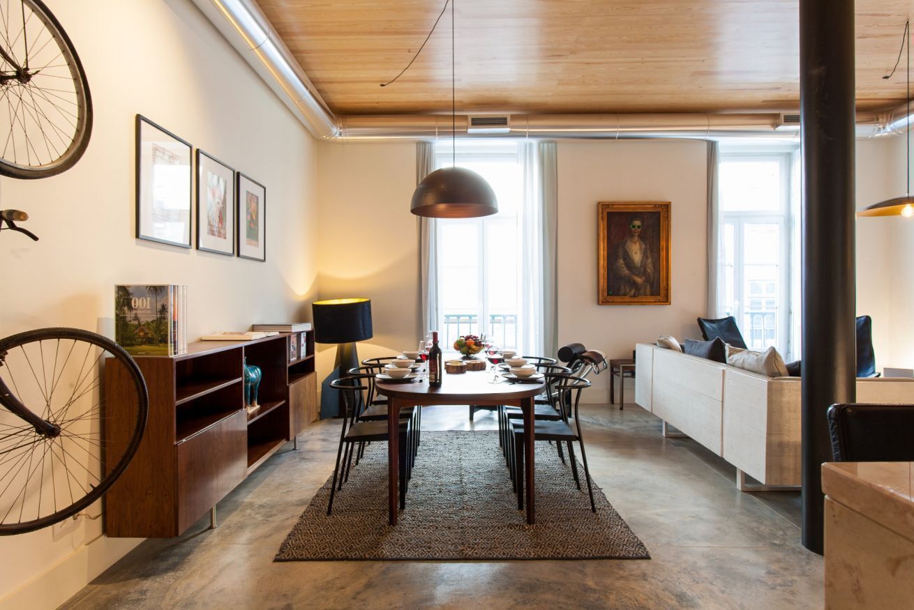 A modern dining area with a round table, chairs, and a rug. There is a bicycle mounted on the wall, a sofa, and a painting on the wall.