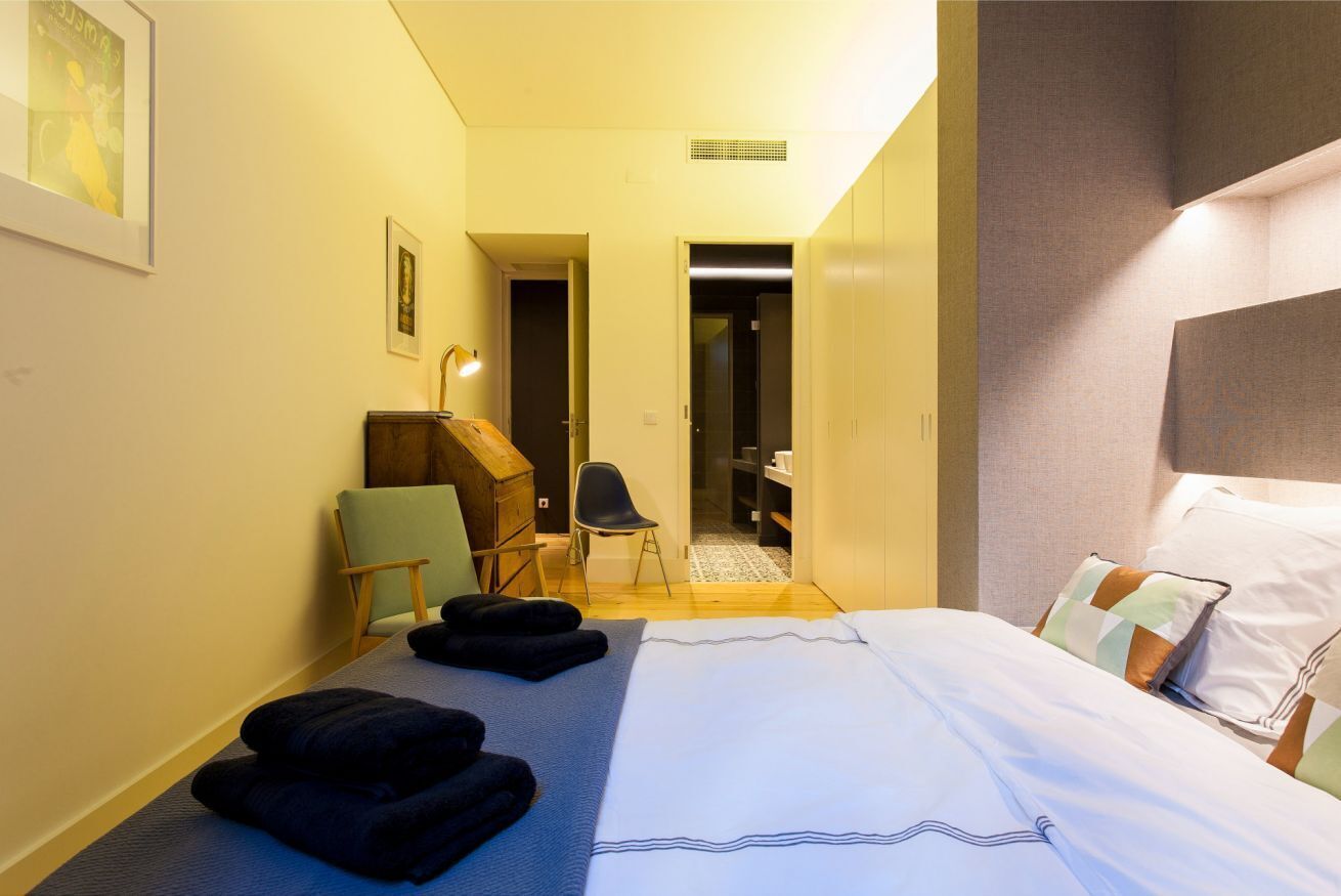 Quarto de hotel com uma cama, escrivaninha, cadeira e guarda-roupa.