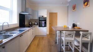 Una cocina moderna con armarios blancos, un lavamanos de acero inoxidable y una mesa de comedor de madera con sillas blancas.