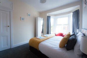 A hotel room with a bed, a window with curtains, a door, and a small picture on the wall. - Ashville Lodge - Five Bedroom House, Sleeps 10 (Scarborough)