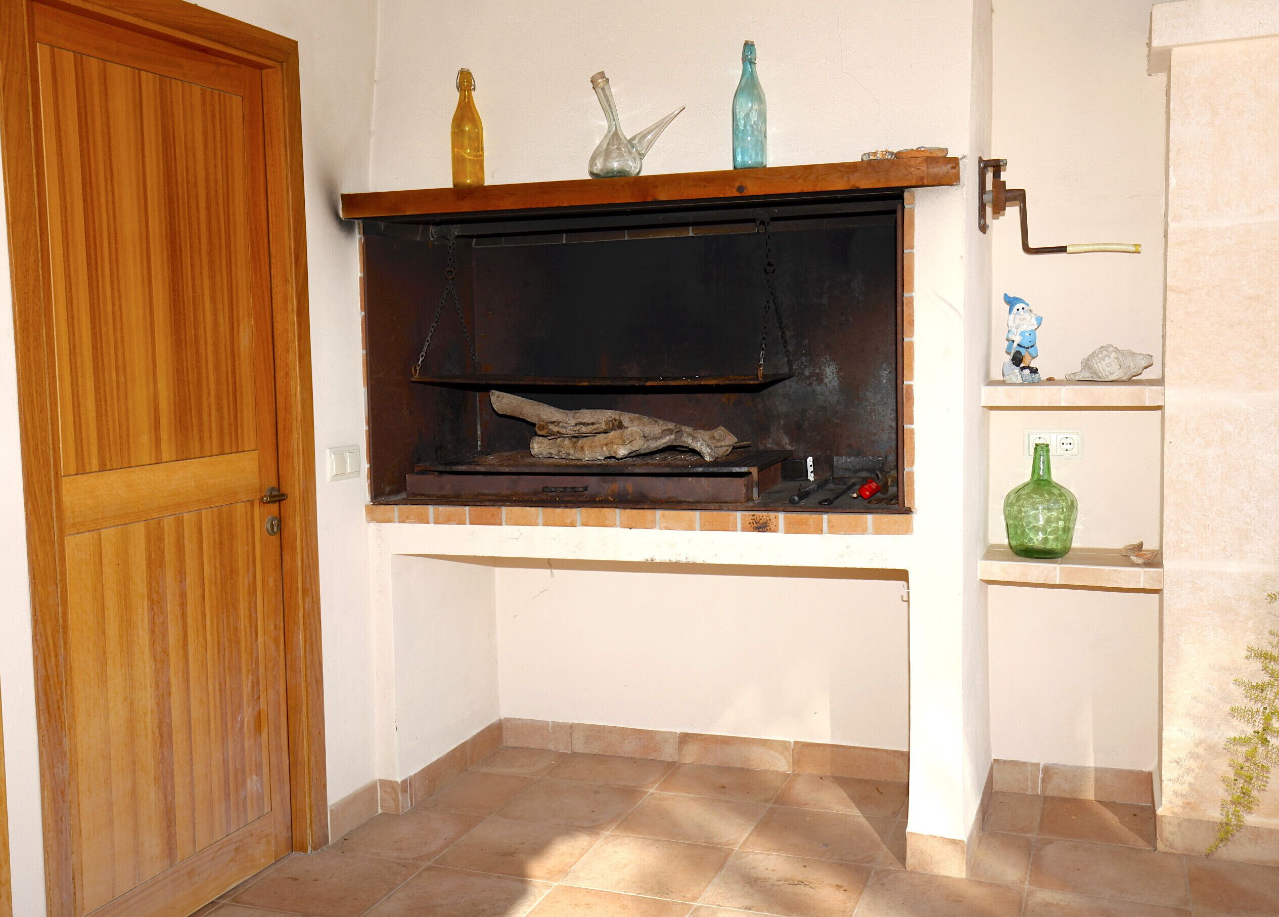 Habitació d'angle amb una porta de fusta, una llar de pedra i prestatges decorats amb objectes ornamentals.