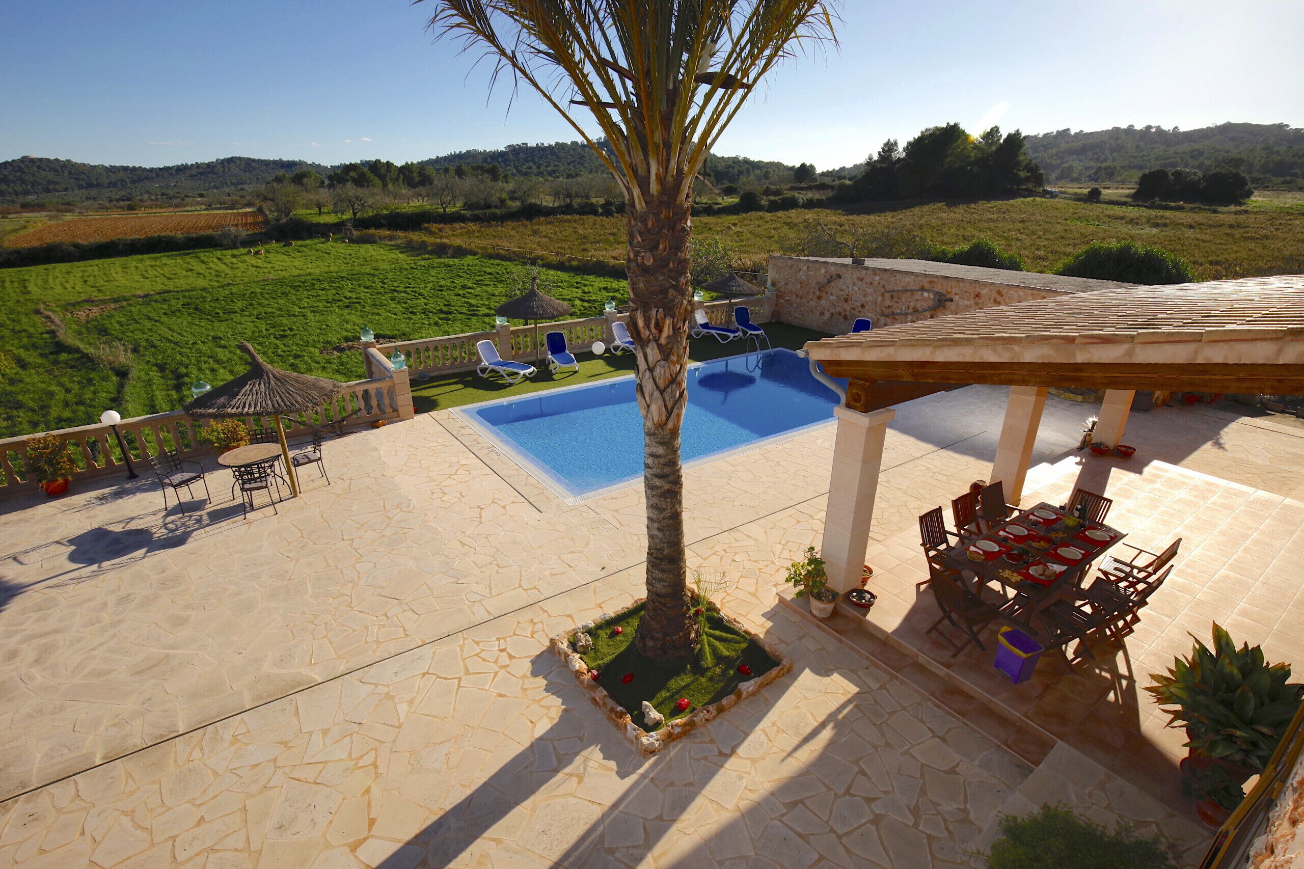 A pool area with lounge chairs, a table, and a view of the countryside.