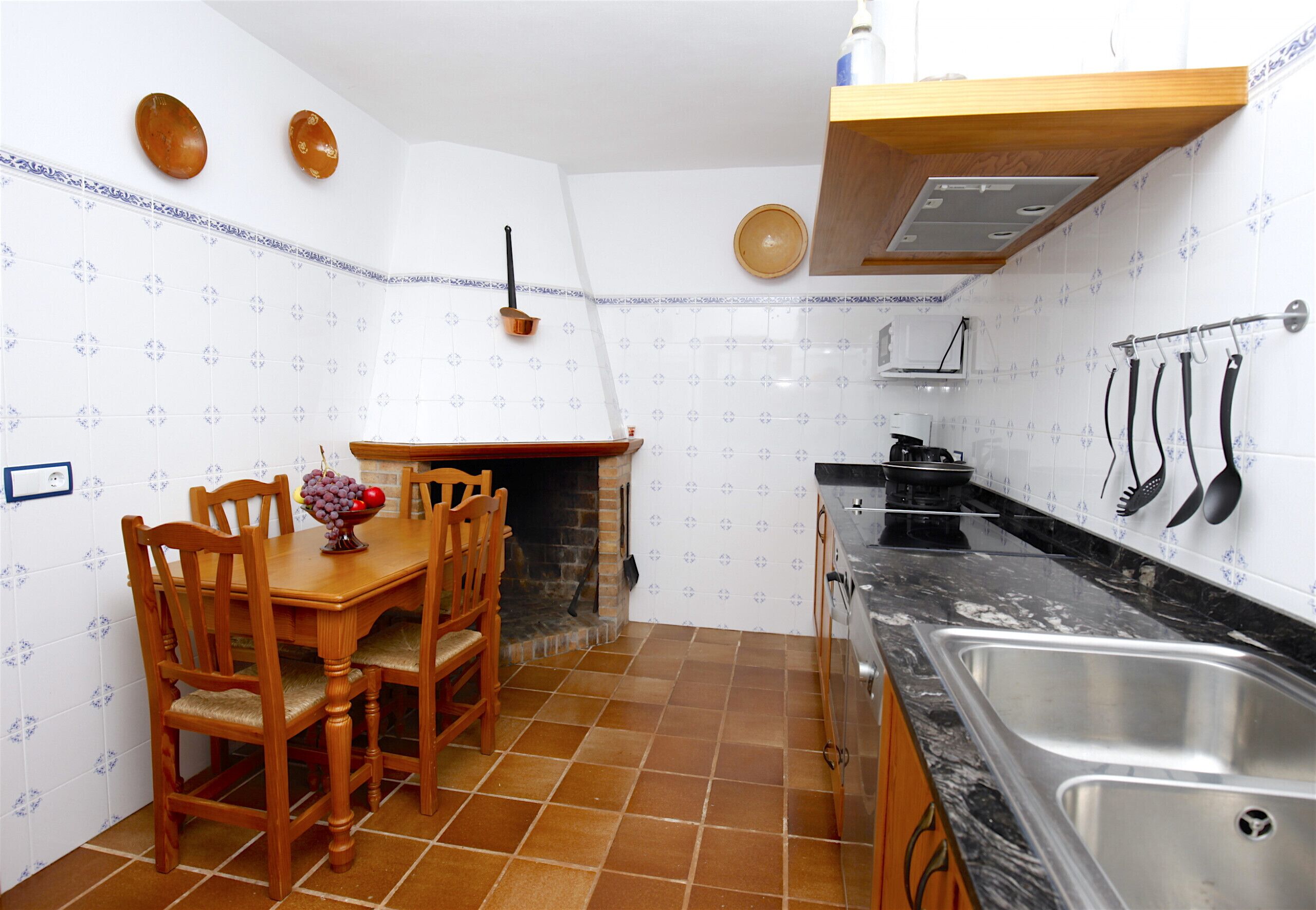 Una cocina compacta con salpicadero de azulejos, sillas de madera, una mesa de comedor, encimera negra y un lavamanos de acero inoxidable.