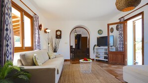 A living room with a sofa, a coffee table, and a TV. There is a wooden door and a window with curtains.