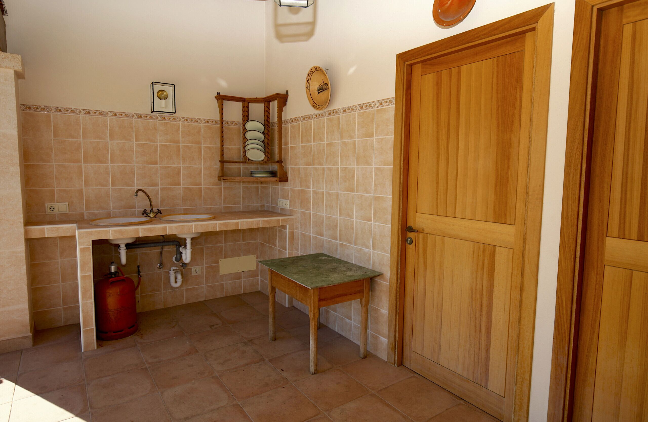 Una cocina compacta con un lavabo, una mesa de madera y un cilindro de gas rojo.